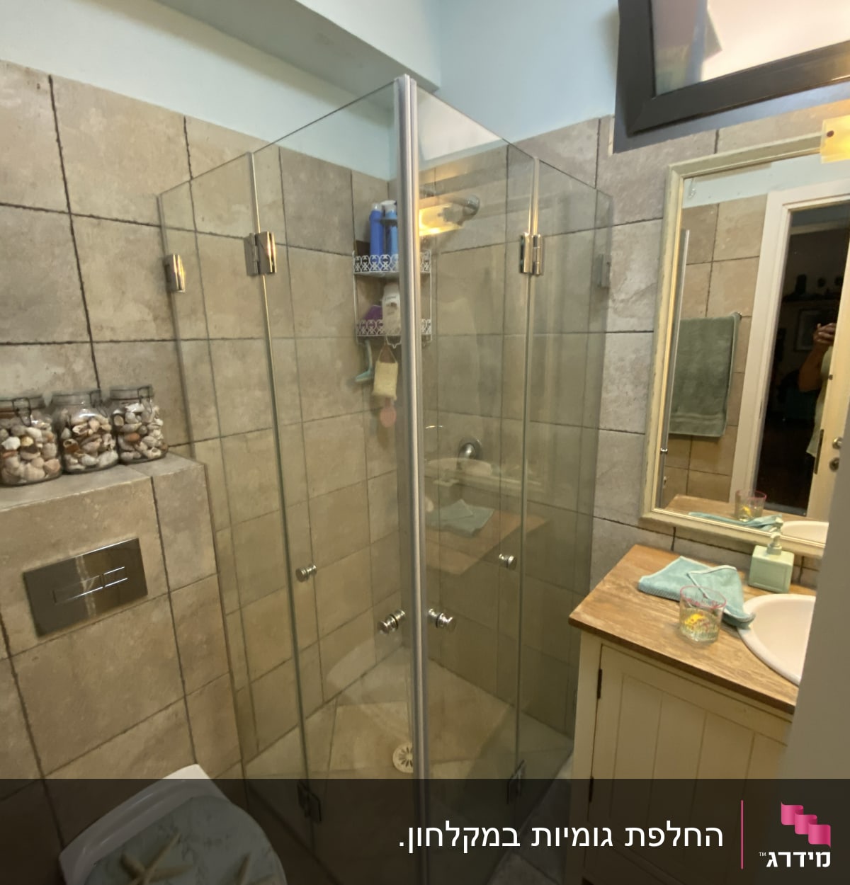 מקלחון זכוכית עם בקבוקי שמפו ומדף